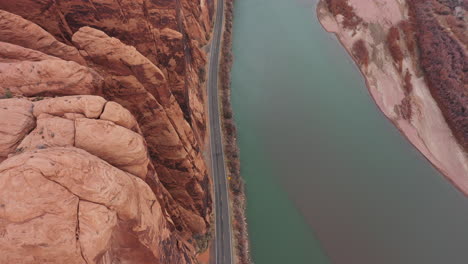 Birds-Eye-Aerial-View-of-Utah-State-Route-Road-by-Colorado-River-Under-Steep-Sandstone-Cliffs