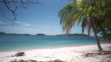 footage-of-white-sand-beach-with-turquoise-waters,-palm-trees-and-islands-in-the-distance