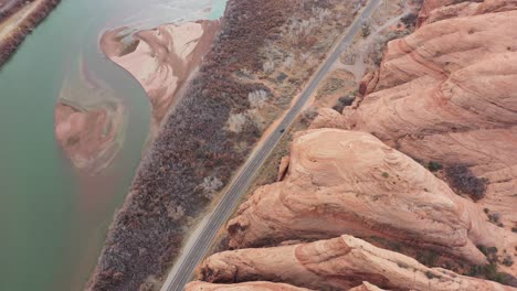Cinematic-Aerial-View-of-Dark-Vehicle-Moving-on-Road-in-Utah-Desert-Landscape-by-Colorado-River-Under-High-Steep-Sandstone-Hills,-High-Angle-Top-Down-Drone-Shot