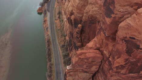 Aerial-View-of-Utah-State-Route-Near-Moab-USA,-Road-by-Colorado-River-Under-High-Steep-Cliffs,-Revealing-Drone-Shot