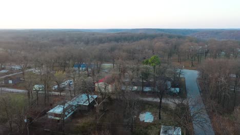 Middle-of-Nowhere-Houses-Surrounded-By-Barren-Forest-Trees-in-Tiny-Rural-Town-with-Backroads-on-Dark-Cloudy-Day---aerial-drone-pullback