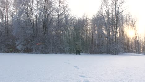 Man-walks-through-deep-snow-in-forest,-side-view