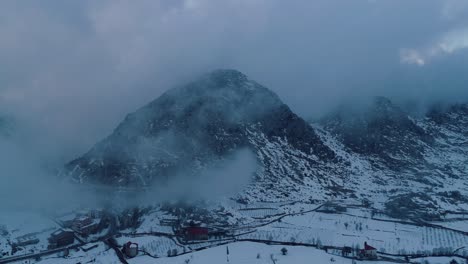 Drone-flying-backwards-through-clouds-revealing-snow-capped-mountain-range-in-Ehmej
