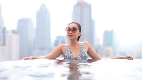 Sexy-asian-woman-in-rooftop-swimming-pool-with-modern-metropolis-cityscape-in-background