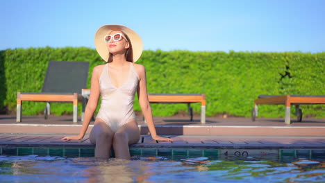 Slim-Woman-in-Swimsuit-Sitting-at-Pool-Border-Enjoying-in-Evening-Sun-on-Tropical-Destination