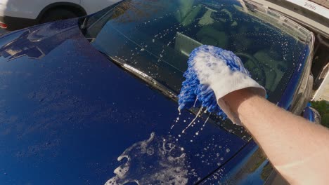 Mans-arm-washing-a-blue-car-with-a-blue-hand-mit