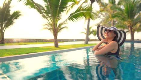 Classy-Asian-Lady-With-Floppy-Summer-Hat-in-Swimming-Pool-on-Tropical-Destination
