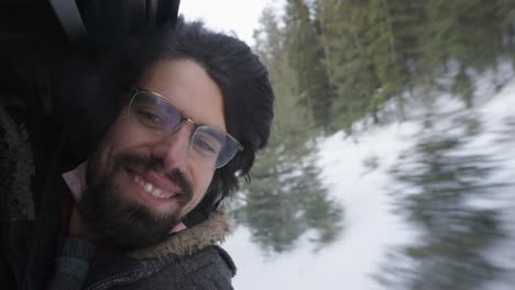 Closeup-portrait-of-happy-enthusiastic-caucasian-man-with-dark-hair-enjoying-sustainable-train-travel-snowy-winter-landscape,-handheld,-slow-motion,-green-traveling