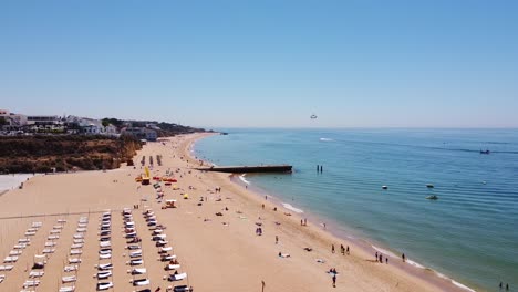 Praia-dos-Alamaes-Beach-at-Albufeira,-Algarve,-Portugal---Aerial-drone-View-of-the-Sandy-Beach-with-Tourists-and-Parasailing-Boat