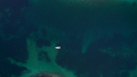 Sail-boat-floating-on-calm-blue-sea-water,-top-down-aerial