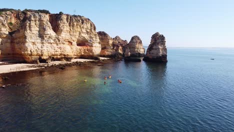 Ponta-Da-Piedade,-Lagos,-Algarve---Aerial-Drone-View-of-Kayakking-Tourists-and-Rocky-Coastline-with-Golden-Cliffs