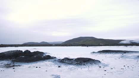 Nahaufnahme-Von-Felsen-In-Einem-Zugefrorenen-See,-Autos-Fahren-Am-Ufer,-Island
