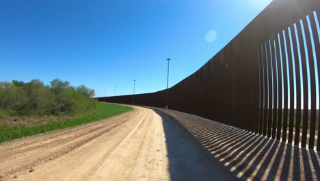 POV-driving-on-service-road-between-a-ditch-and-border-wall-between-USA-and-Mexico