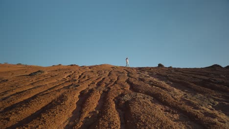 Distant-woman-walking-on-ridge-of-erosion-shaped-landscape-on-sunny-day