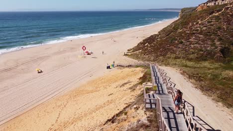Praia-Das-Bicas-Beach-at-Castelo,-Alentejo,-West-Coast-Portugal---Aerial-Drone-View-of-a-Tourist-Girl-walking-the-Staircase-to-the-Golden-Sandy-Beach