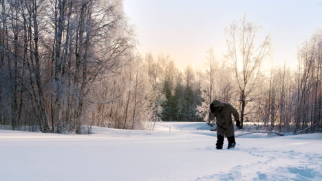 Vista-Estática-De-Un-Hombre-Con-Un-Abrigo-Pesado-Caminando-A-Través-De-La-Nieve-Profunda-En-Un-Parque-Congelado