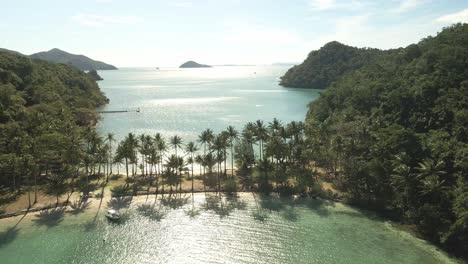 forward-aerial-dolly-of-tropical-island,-sand-bar-white-sand-beach,-palms-backlit-with-sunrise
