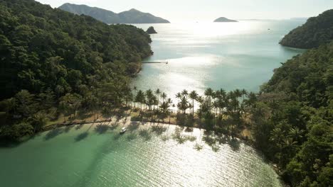 Aerial-of-tropical-island-joined-by-a-sand-bar-beach-with-palm-trees-and-shadows-of-palms-on-the-ocean-in-Thailand