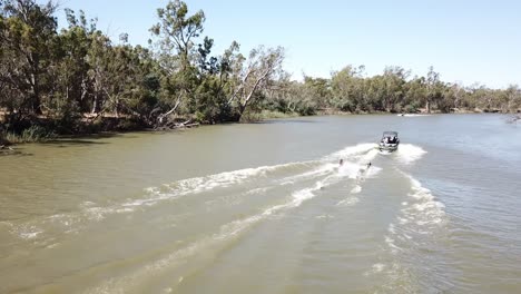 Drohnenantenne-über-Dem-Fluss-Mit-Boot-Und-Zwei-Wasserskifahrern