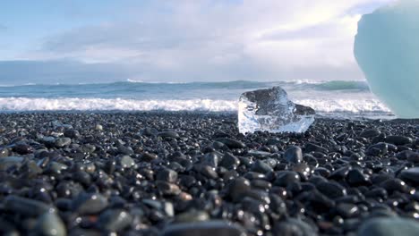 Small-piece-of-ice-on-pebbles,-Diamond-beach-in-Iceland-with-sea-waves