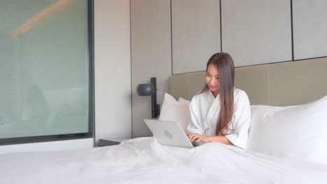 Hübsche-Asiatische-Frau-Im-Bett,-Die-Am-Hellen-Morgen-E-mails-Auf-Laptop-computer-Tippt-Und-Sendet