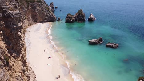 Strand-Praia-Ribeira-Do-Cavalo-In-Der-Nähe-Von-Sesimbra,-Alentejo,-Portugal---Luftdrohnenansicht-Der-Felsigen-Küste,-Des-Paradiesischen-Sandstrandes-Und-Des-Türkisfarbenen-Meeres
