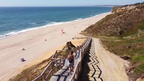 Praia-Das-Bicas-Beach-at-Castelo,-Alentejo,-West-Coast-Portugal---Aerial-Drone-View-of-a-Tourist-Girl-walking-the-Stairs-to-the-Golden-Sandy-Beach