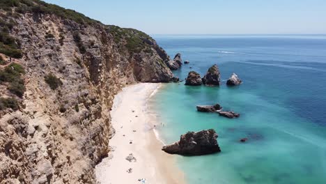 Strand-Praia-Ribeira-Do-Cavalo-In-Der-Nähe-Von-Sesimbra,-Alentejo,-Portugal---Drohnenansicht-Der-Steilküste-Mit-Verstecktem-Paradiesstrand-Und-Türkisfarbenem-Meer