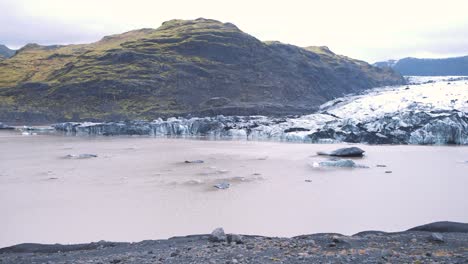 Rocks-and-ice-in-frozen-lake-in-Solheimajokull-glacier-valley,-Iceland