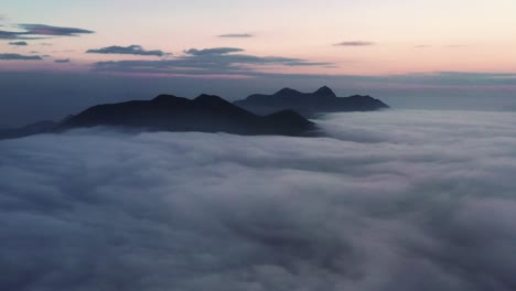 Aerial-dolly-in-of-dense-layer-of-clouds-over-Hong-Kong-Island,-covering-mountain-tops-at-blue-hour-in-Kowloon-Peak,-China
