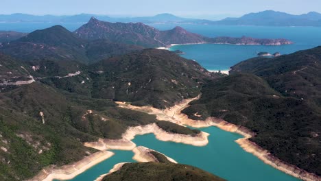 Aerial-dolly-in-of-High-Island-Reservoir-verdant-hills-rock-columns-in-shore-and-turquoise-water,-San-Kung-Peninsula-in-Hong-Kong,-China