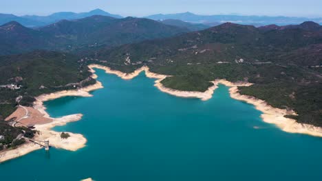 Aerial-pan-right-of-High-Island-Reservoir-turquoise-water,-sand-beach-shoreline-and-verdant-hills,-San-Kung-Peninsula-in-Hong-Kong,-China