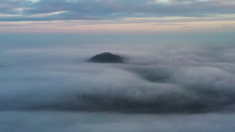 Aerial-orbit-over-mountain-top-almost-covered-by-dense-layer-of-clouds-at-overcast-blue-hour-in-Kowloon-Peak,-Hong-Kong,-China