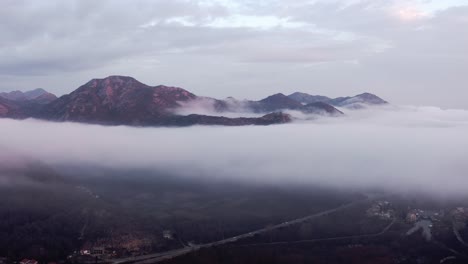 AERIAL---Low-clouds-above-a-mountain-village-at-Lake-Skadar,-Montenegro,-forward