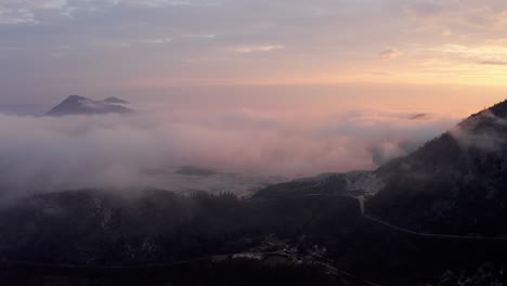 AERIAL---Low-clouds-at-sunrise-in-mountain-village-at-Lake-Skadar,-Montenegro