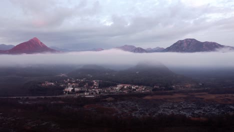 AERIAL---Low-clouds-above-mountain-village-at-Lake-Skadar,-Montenegro,-forward