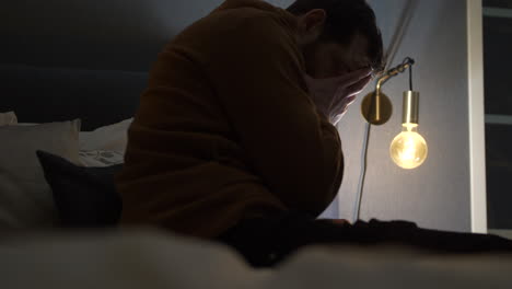 Stressed-man-with-headache-sits-on-edge-of-bed-at-night