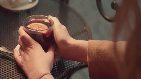 Cup-of-mulled-wine-and-warming-female-hands-holding-steaming-mug,-outside-closeup-view