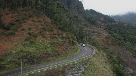 Car-drives-around-blind-corner-on-high-mountain-pass,-winding-road,-aerial