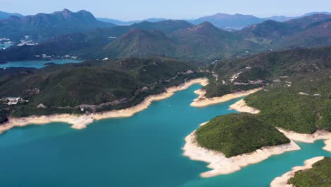 Aerial-truck-left-of-High-Island-Reservoir-turquoise-water-sand-beach-shoreline-and-verdant-hills,-San-Kung-Peninsula-in-Hong-Kong,-China