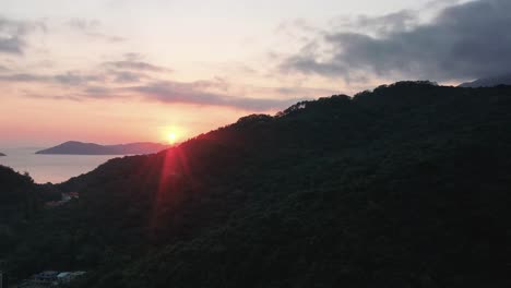 Aerial-Truck-Links-Von-Sonnenstrahlen-Des-Sonnenuntergangs-Hinter-Regenwaldhügeln-Und-Dorf-In-Pui-O-Bay,-Meer-Im-Hintergrund,-Insel-Lantau,-Hongkong,-China