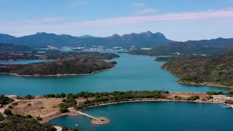 Aerial-flying-over-High-Island-Reservoir-turquoise-water,-verdant-hills-and-trails-at-daytime,-San-Kung-Peninsula-in-Hong-Kong,-China