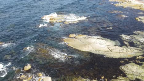 Drone-aerial-pan-down-to-show-tropical-blue-water-crashing-on-rocks-Tasmania