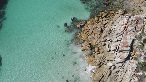 Drone-aerial-slow-moving-forward-over-beach-with-tropical-blue-water-and-rocks-on-sunny-day