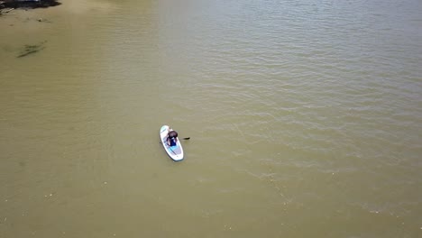Drone-aerial-over-river-woman-trying-to-stand-up-on-paddle-board
