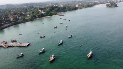 Umlaufbahnaufnahme-Einer-Großen-Anzahl-Von-Fischerbooten-Mit-Grüner-Landschaftsbucht,-Weligama-Sri-Lanka