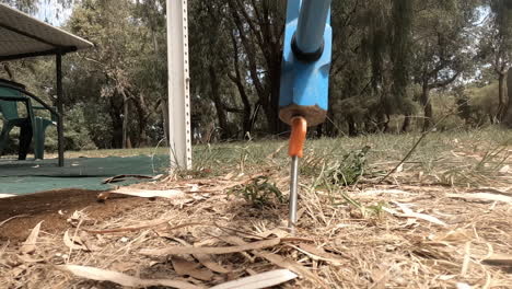 Hammering-an-orange-tent-peg-in-the-dry-ground-with-a-blue-hammer