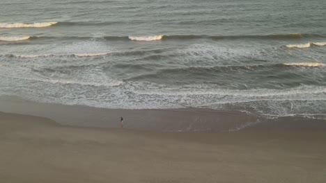 Luftdrohne-Umkreist-Eine-Isolierte-Person,-Die-Bei-Sonnenuntergang-Am-Strand-Spazieren-Geht,-Playa-La-Viuda-In-Uruguay