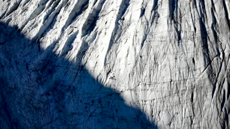 Aerial-flyover-over-Morteratsch-glacier-in-Engadin,-Switzerland-at-dawn-with-a-pan-up-towards-some-of-the-tallest-peaks-of-the-Swiss-Alps-like-Piz-Bernina,-Piz-Palu