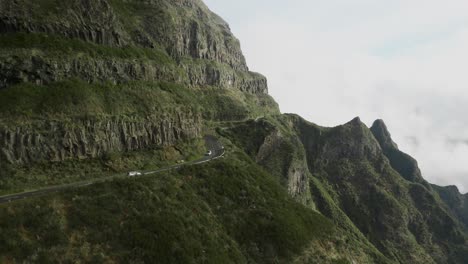 Two-cars-travelling-in-opposite-direction-and-cross-each-other-on-winding-mountain-road-in-Madeira,-aerial